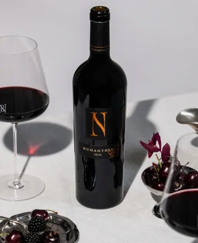 Bottle of Numanthia Spanish red wine from Bodega Numanthia on a table with a wine glass, red berries and silver cutlery.