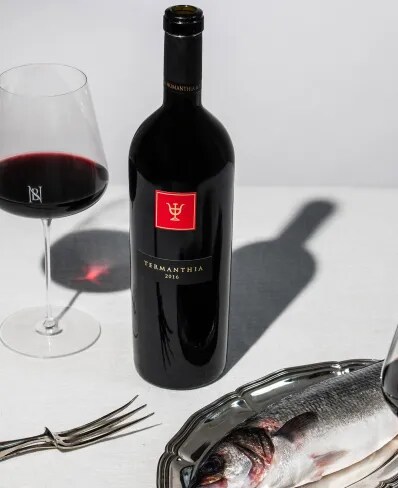 Botella de vino tinto español Termanthia de Bodega Numanthia sobre una mesa con una copa de vino, un pescado y cubiertos de plata.