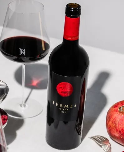 Bottle of red spanish Wine Termes of Bodega Numanthia on a table with a glass of wine, a pomegranate, and silver cutlery